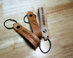 Leather EDC keychains in veg tan and bourbon with engraved Bigfoot Forge branding and steel cable rings