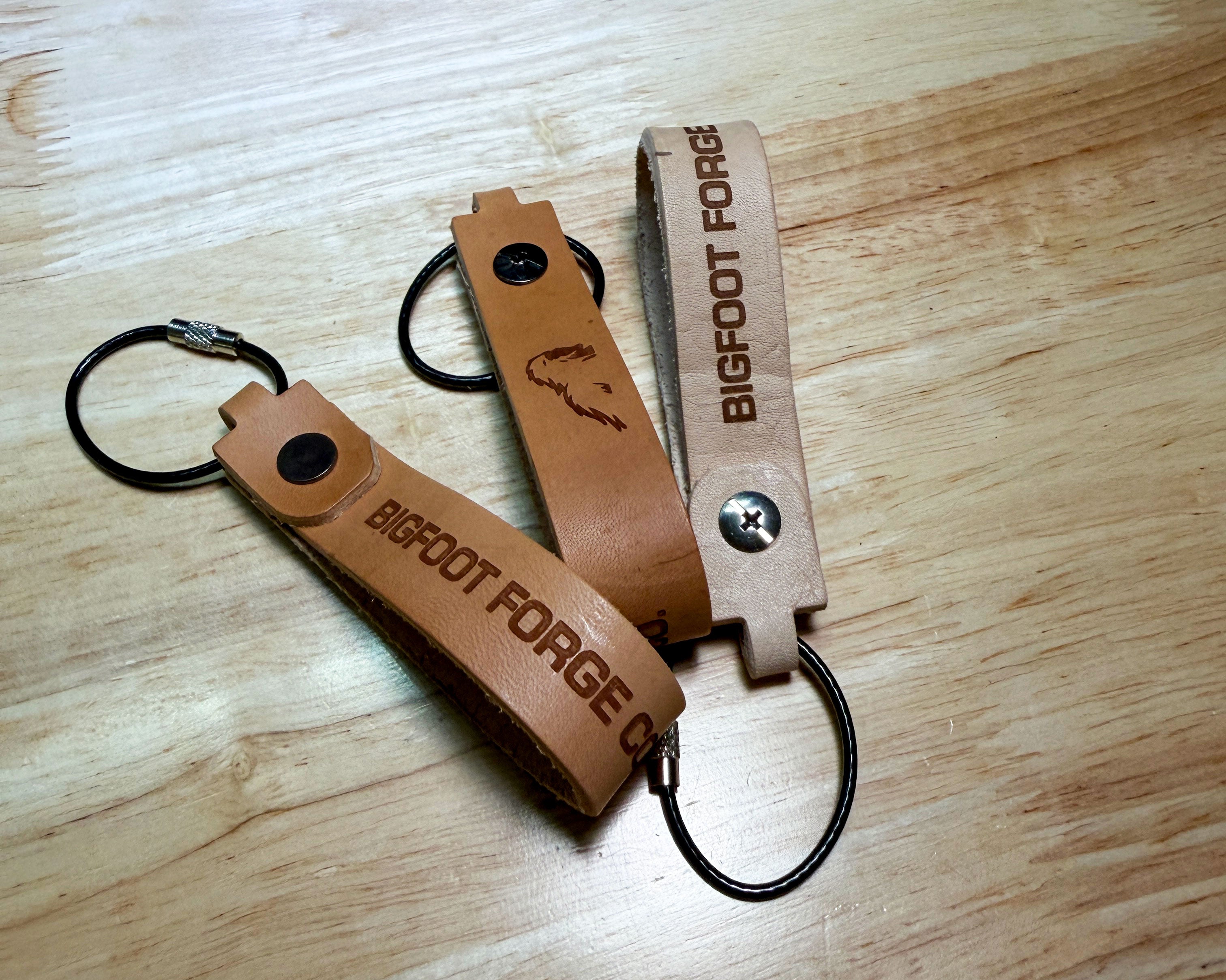 Leather EDC keychains in veg tan and bourbon with engraved Bigfoot Forge branding and steel cable rings