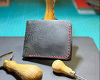 Angled view of a black Topo leather bifold wallet with red stitching