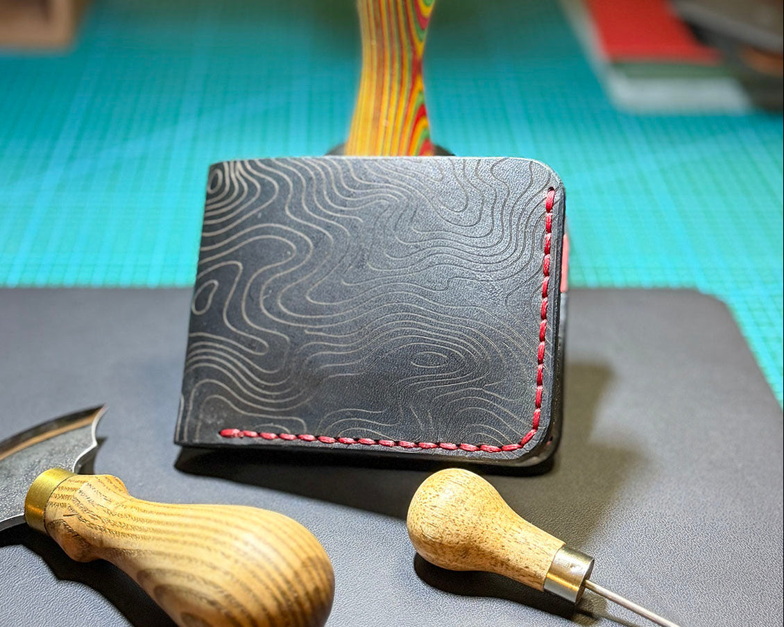 Angled view of a black Topo leather bifold wallet with red stitching