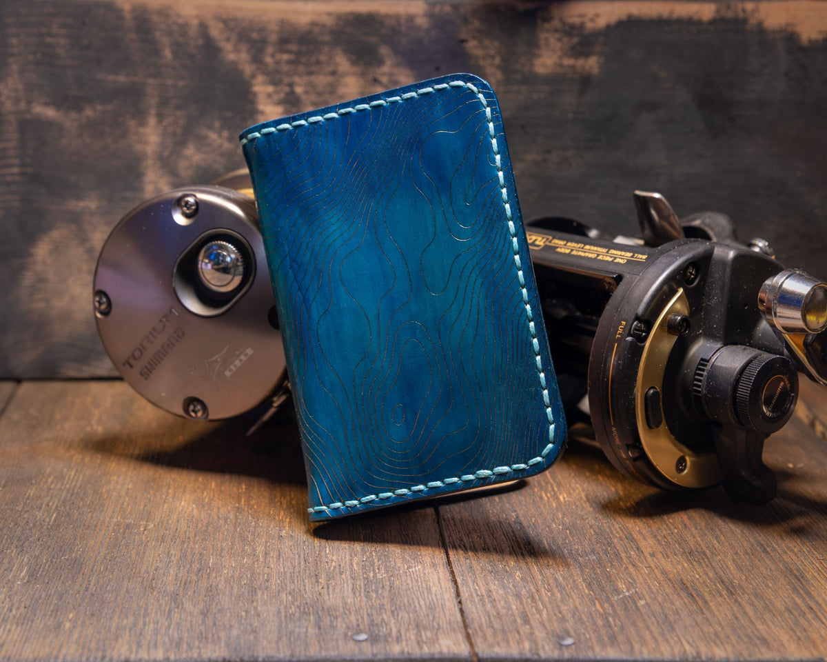 Forgehand Field Deep Blue Water vertical leather wallet with hand-dyed blue gradient, topo engraving and light contrast stitching.